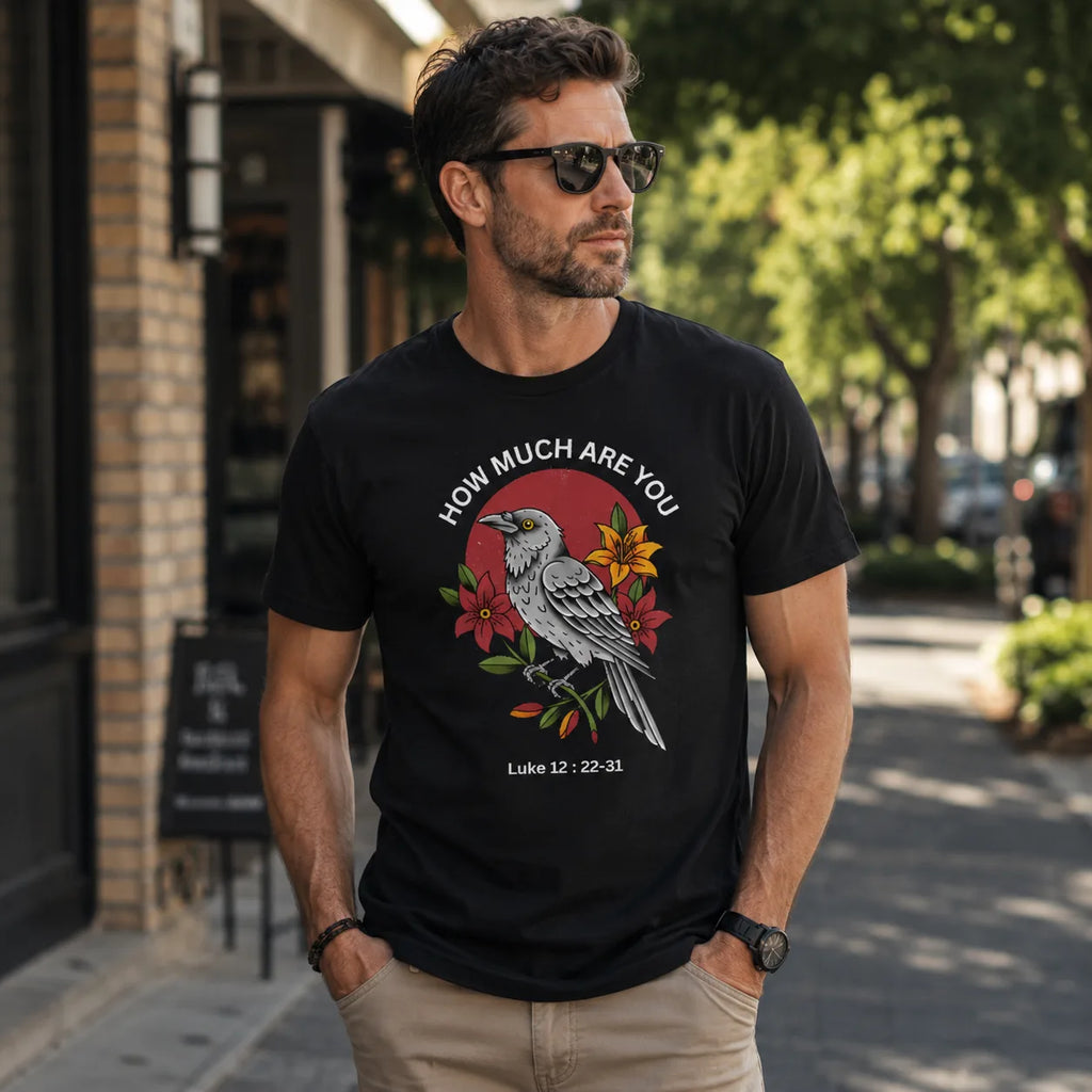 A man wearing a black graphic t-shirt with a bird and floral design and the text 'HOW MUCH ARE YOU Luke 12: 22-33' on a city street.